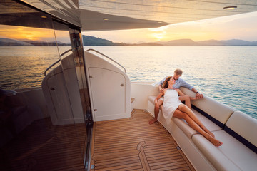 Romantic vacation and luxury travel. Young loving couple sitting on the sofa on the modern yacht deck. Sailing the sea. - obrazy, fototapety, plakaty