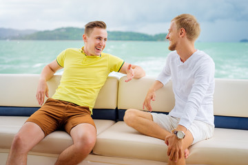 Friendship and vacation. Two young handsome men talking on tha yacht sailing the sea.