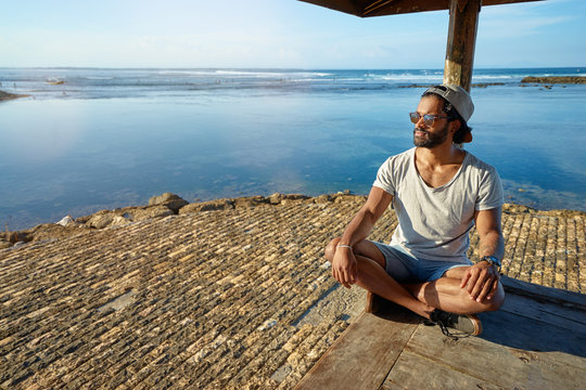 Relaxed and cheerful. Outdoor portrait of happy young african man resting on deck near the sea.