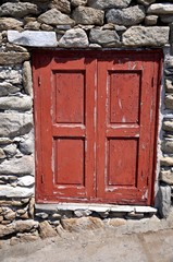 Ventana roja de madera deteriorada en pared de piedra