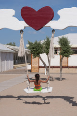 Little girl on a rope swing on the equipped beach. Summer, beach resort