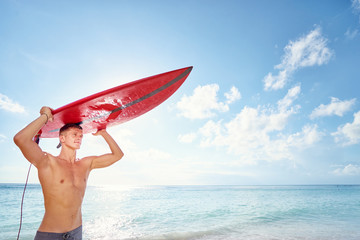 Naklejka na ściany i meble Hobby and vacation. Sunny holiday on the beach. Young man carruing surf board.
