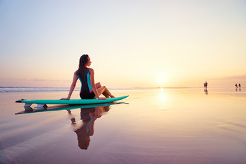 Surfing and vacation. Holiday on the beach. Relaxed young woman siiting on the sand with surf board...