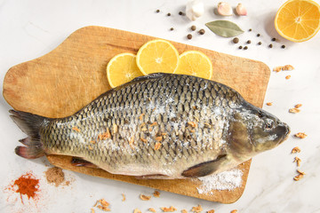 Raw fresh fish (carp) with lemon, garlic and spices on wooden cutting board on light vintage background with copy space. Healthy food and cooking.