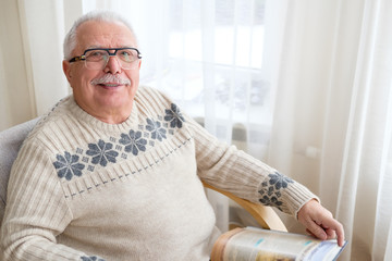 Senior man 75-75 years old sitting at home and reading book in armchair. Old age, lifestyle and people concept