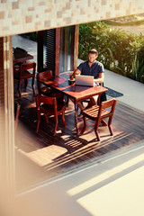 Freelance concept. Young  bearded man working on laptop computer while sitting on cafe terrace.