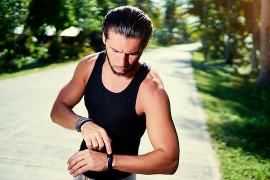 Healthy lifestyle and technology. Young handsome strong man using smart watch tracker outdoors.