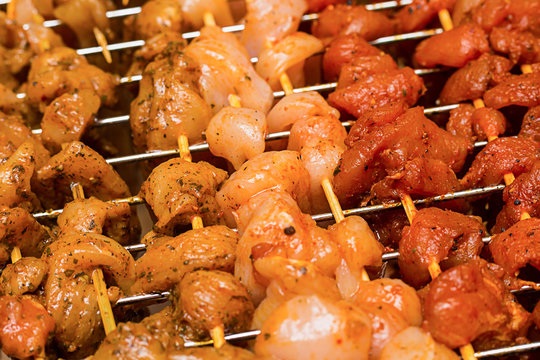 parallel wooden skewers with chicken and pork with curry and paprika on the background of metal grilling
