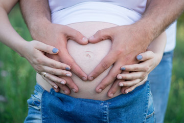 men's hands carefully embrace the belly of a pregnant wife in garden