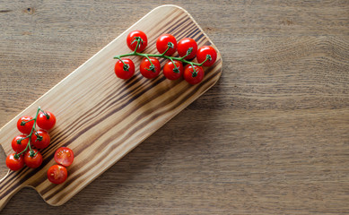 A branch of cherry tomatoes on wooden cutting board. selective focus. top view. pattern with place for text  pattern with place for text