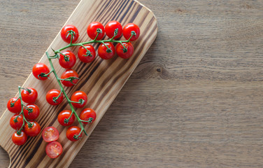 A branch of cherry tomatoes on wooden cutting board. selective focus. top view. pattern with place for text