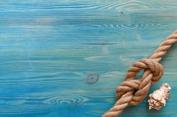 Summer vacation background with copy space. Sea rope knot and seashell on blue wooden table...