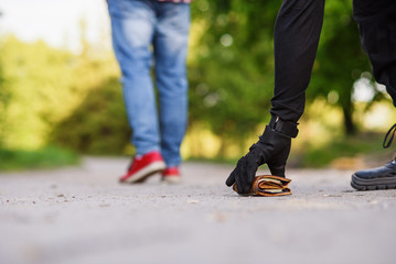 The thief in black clothes raises a wallet with money from the ground. Pickpocketing on the street during daytime.