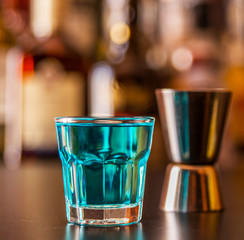 Popular blue drink shot kamikaze on the background of the bar with bottles, a refreshing drink
