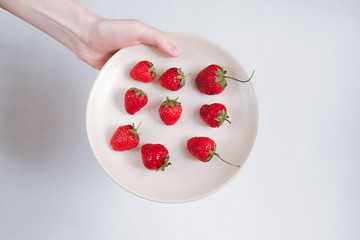 Female hand holding  pink dish with strawberries on white background
