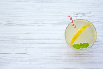 Lemonade drink in a glass with fresh lemon and mint over white wooden background, top view. Copy space.