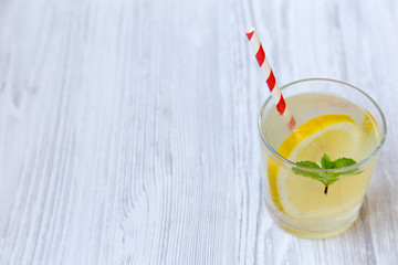 Lemonade drink in a glass with fresh lemon and mint over white wooden background, side view. Copy space.