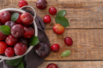 Colander with ripe juicy plums on wooden table