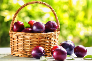 Wicker basket with ripe juicy plums on table