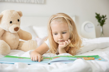 Cute girl reading book on bed at home