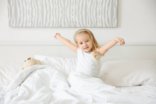 Cute little girl stretching in bed at home