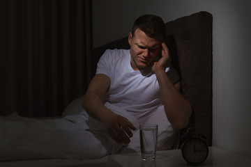 Fototapeta premium Young man with terrible headache want to take pill at night