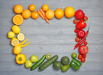 Frame made of ripe fruits and vegetables in rainbow colors on grey background, top view
