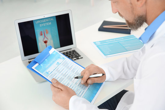 Mature Urologist Working At Table In Hospital