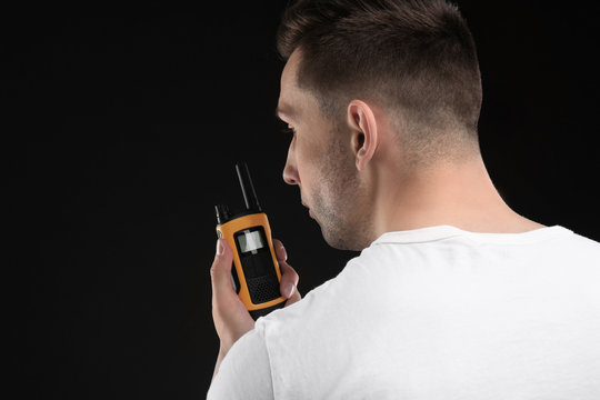 Male security guard using portable radio transmitter on dark background