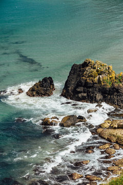 A cliff-top view of the Irish sea and rugged shore on a bright sunny day. Large rocks protrude from the water.