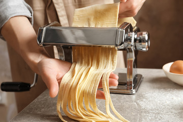 Young woman preparing noodles with pasta maker at table