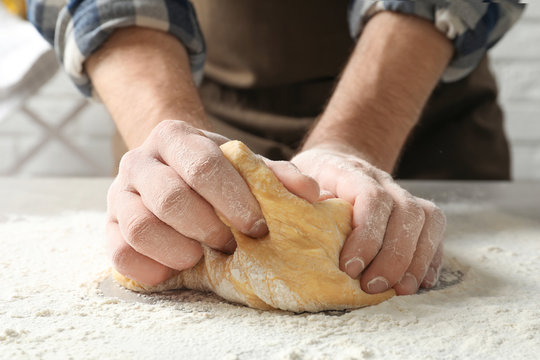 Young man kneading dough for pasta on table