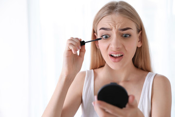 Emotional woman with eyelash loss problem applying mascara indoors