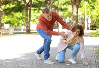 Man helping mature woman suffering from heart attack in park