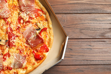 Carton box with delicious pizza on wooden background, top view
