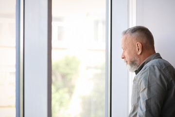 Fototapeta premium Depressed senior man near window indoors