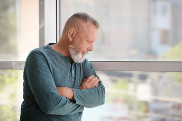 Naklejka premium Depressed senior man near window indoors