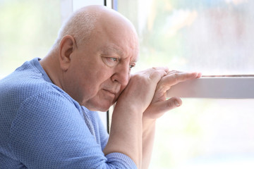 Depressed senior man near window indoors