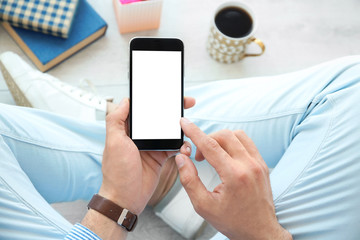 Young man holding mobile phone with blank screen in hand, indoors