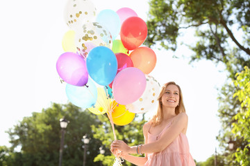 Young woman with colorful balloons outdoors on sunny day