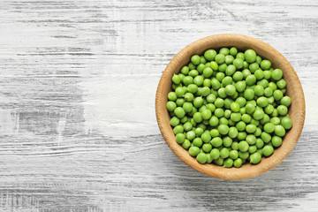 Plate with green peas on wooden background, top view