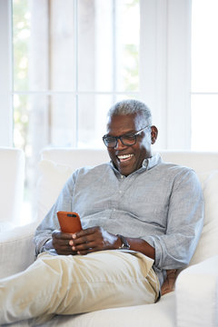 African American Senior man texting on a smart phone sitting on the couch at home