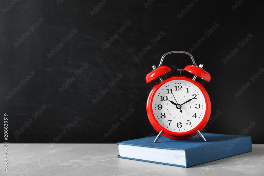 Poster Alarm clock with book on table against color background. Time concept