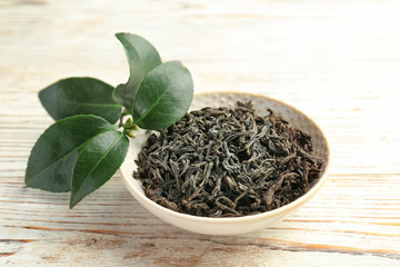Plate with dry tea and fresh green leaves on table