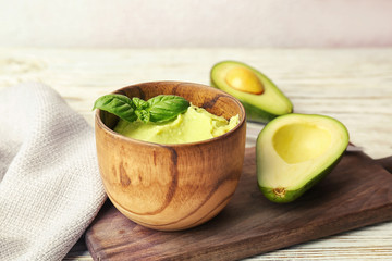 Bowl with guacamole and ripe avocado on table