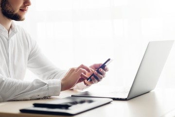 Young smiling bearded businessman is working on computer holding