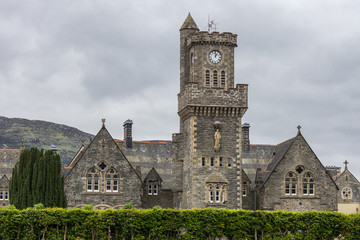 Fort Augustus, Scotland - June 11, 2012: Closeup of the Abbey Highland Club with clock tower fronted by garden  under heavy cloudscape. Hills on horizon.