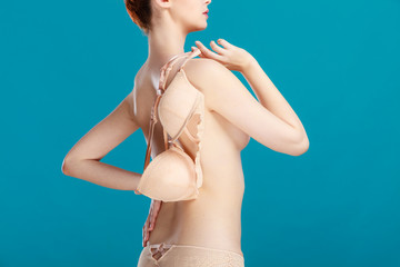 Naked woman holds beige bra in hand