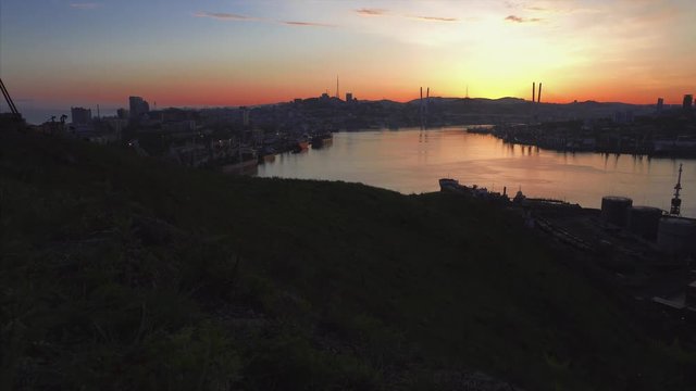Panorama view of Vladivostok center, flying backwards above the Golden Bridge (cable-stayed bridge built in 2012 across the Zolotoy Rog harbour), view of cars driving along it. Russia