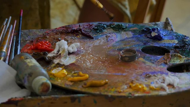 Wooden art palette with oil paints. Mixing colors together. Artistic instrument with many colors. Working tool with squeezed out tubes of paint.